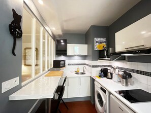 Uma cozinha compacta com máquina de lavar, micro-ondas, pia e relógio na parede.
