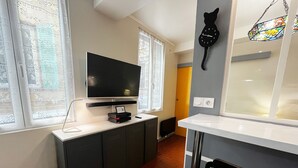 Cocina compacta con televisión de pantalla plana, un refrigerador pequeño y un ventanal con cortinas decorativas.