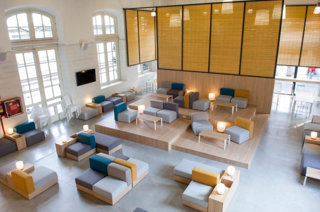 Un área de estar moderna con diversas opciones de asientos, incluyendo sofás y sillones, dispuesta en un espacio amplio con ventanas grandes que ofrecen luz natural.