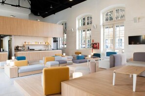 Un intérieur moderne avec un bar, des espaces aménagés pour s’asseoir et de grandes fenêtres.
