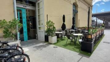 Une auberge de jeunesse avec une enseigne indiquant « UP! HOSTEL » et une porte verte. Des vélos sont garés à l’extérieur, et un petit espace extérieur aménagé avec des tables et des chaises invite à la détente.