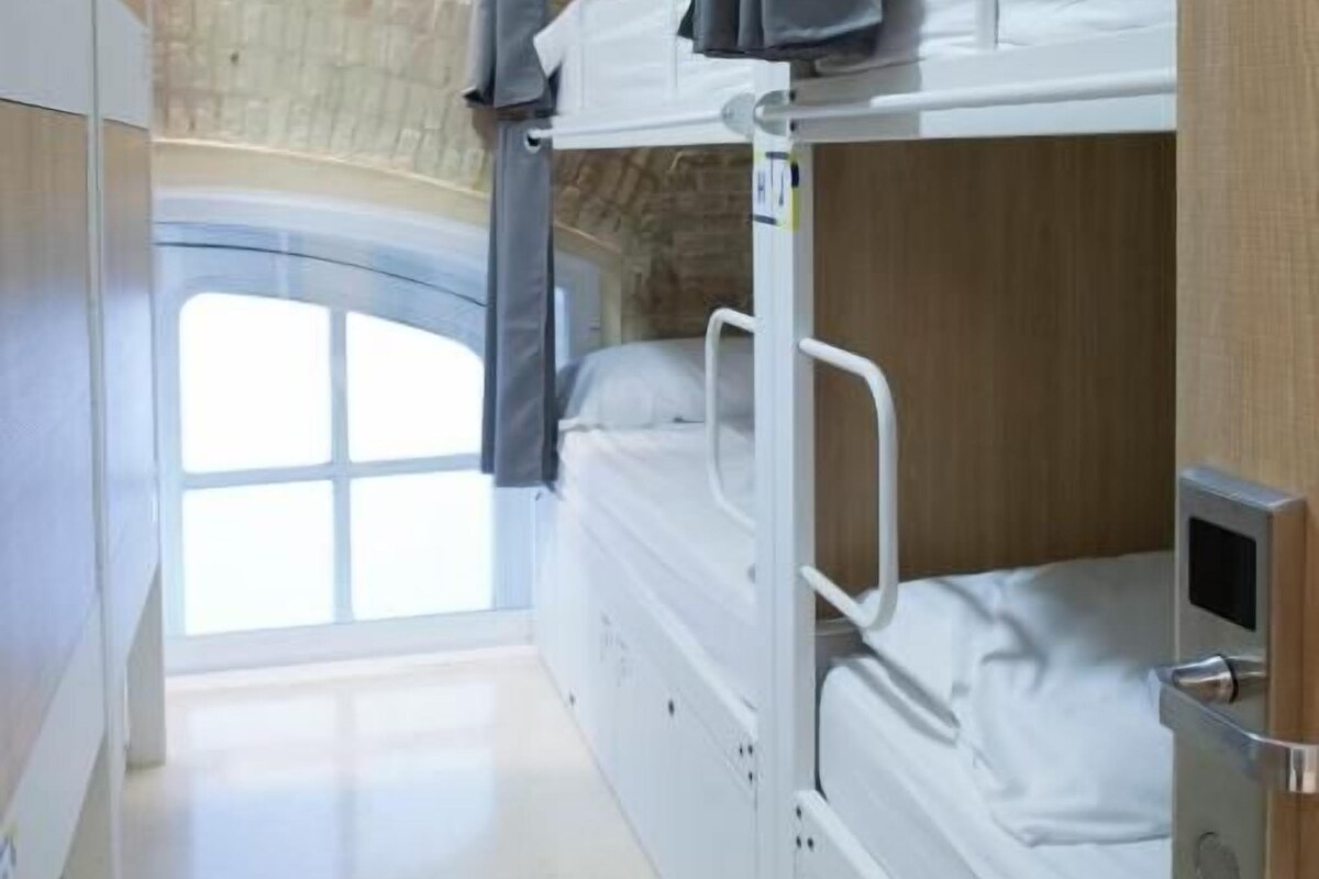 Une chambre avec un lit superposé, une fenêtre, une porte et un mur en pierre.