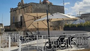 A stone building with a dome and spire, a covered outdoor seating area with metal railings, and a clear blue sky. - Wonderful Maltese Character 1-bedroom with AC in charming Ħal Tarxien (Ħal Tarxien)