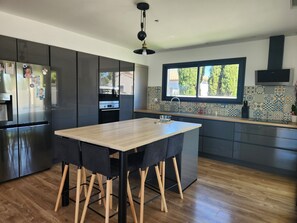 A modern kitchen with a wooden table, dark cabinets, and a window with a view. - Magnificent modern villa with private pool (Sérignan)