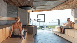 Uma sauna com bancos de madeira, piso de pedra e vista para o mar.