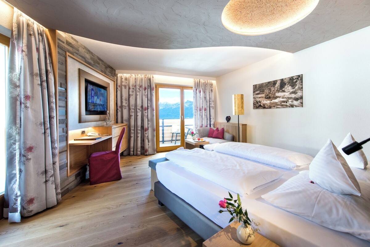Ein Hotelzimmer mit Bett, Schreibtisch, Stuhl, Fernseher und Blick auf die Berge.