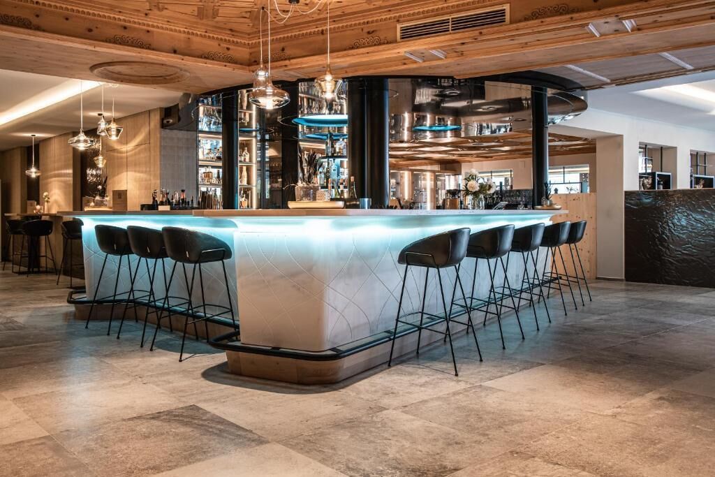 A bar area with a long counter, multiple stools, hanging lights, and a visible bar stocked with bottles.