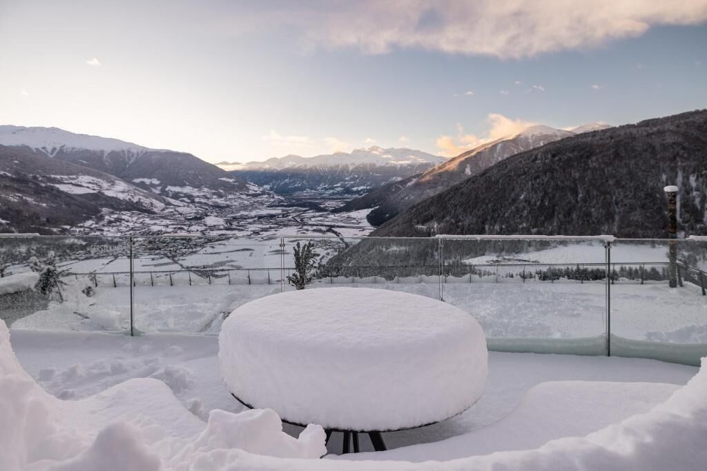 A snow-covered outdoor seating area with a view of a valley and mountains.