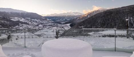 A snow-covered outdoor seating area with a view of a valley and mountains.