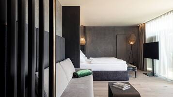A modern hotel room with a large bed, a sofa, a coffee table, and a television.