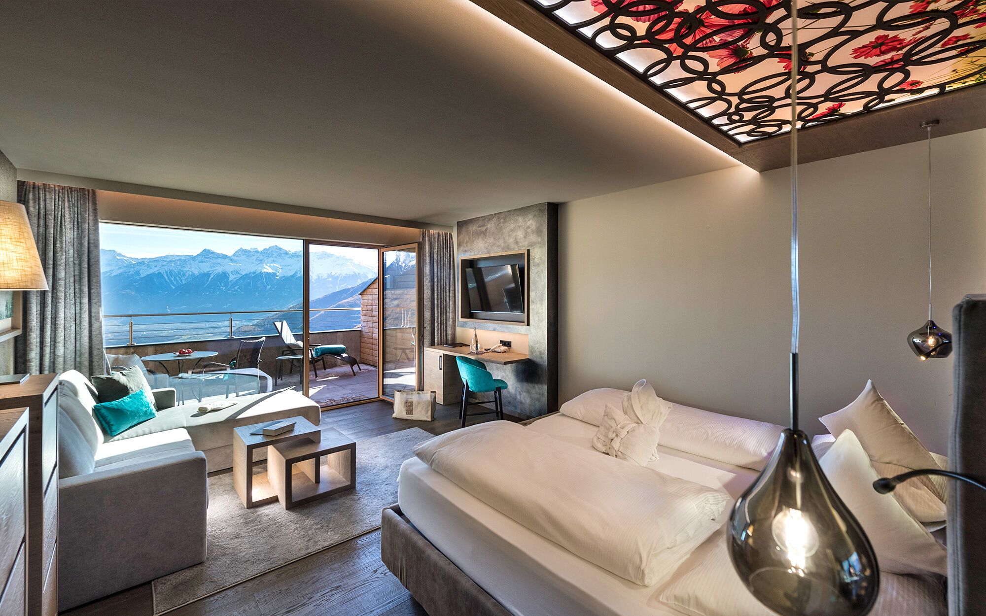 Una habitación de hotel con cama, escritorio, silla, televisor y vista a las montañas.