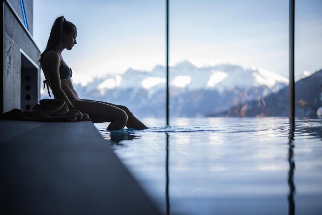 Une personne assise au bord d’une piscine, avec une vue sur les montagnes.