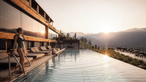 Área de piscina com espreguiçadeiras, deck de madeira e vista para montanhas.