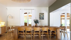 A dining area with a long wooden table, chairs, a floor lamp, and a vase with flowers.