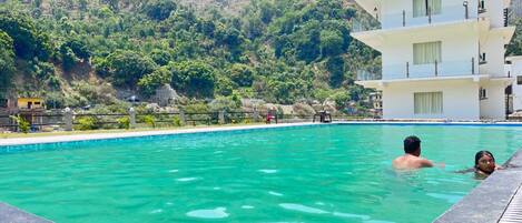 A swimming pool with a view of a mountainous landscape, a multi-story building, and a clear sky.