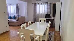 En matplats med ett vitt bord och stolar, en mönstrad matta och en soffa i bakgrunden.