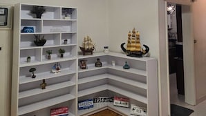 Ett hörnrum med vita hyllsystem där olika dekorativa föremål visas, en svart hängande lampa och ett trägolv med fiskbensmönster.
