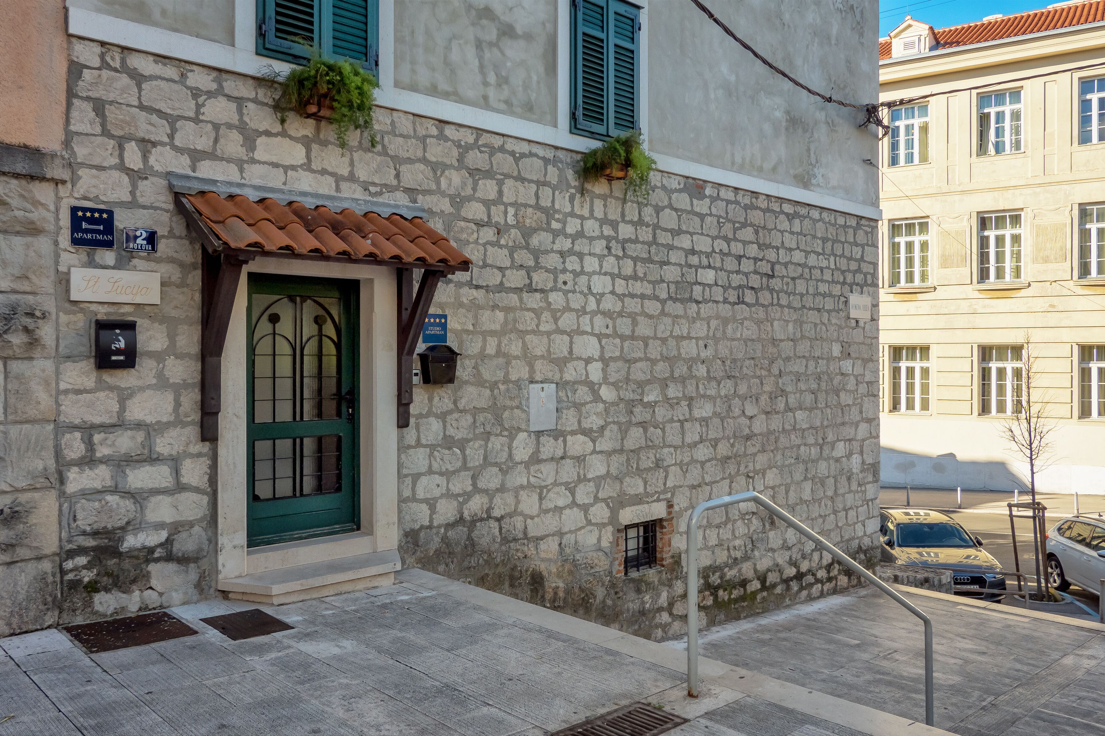 A stone building with a green door, a sign indicating '2 stars,' and a small window with a plant.