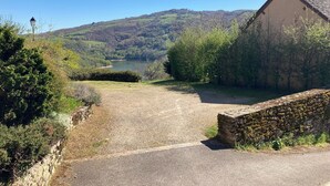 Un paysage rural avec un mur de pierres, un bâtiment doté d’un toit en tuiles et une vue dégagée sur une vallée et des collines.