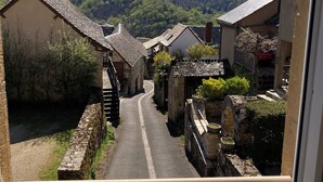 Une rue étroite bordée de bâtiments traditionnels en pierre, un ciel dégagé et une colline lointaine.