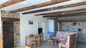 Un intérieur rustique avec des poutres apparentes, un mur en pierre, une table en bois, un canapé et un téléviseur.