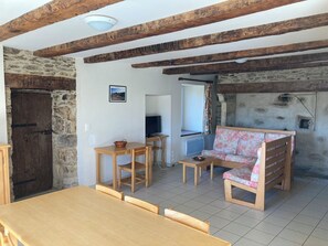 Ein rustikales Interieur mit freiliegenden Holzbalken, einer Steinwand, einem Holztisch, einer Couch und einem Fernseher.