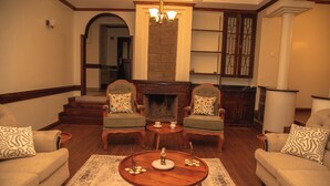 A living room with two armchairs, a coffee table, a fireplace, and a staircase leading to another room. - Mt. Kenya View Villa 5BR Ensuite Guest Wing (Nyeri)