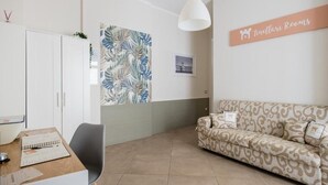 Une pièce avec une armoire blanche, un canapé à motifs, un bureau avec une chaise et un panneau fixé au mur sur lequel on peut lire : « Tinellari Rooms ».