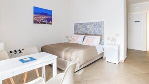 Une chambre d’hôtel comprenant un lit, un bureau, des chaises, une table de chevet et un tableau accroché au mur.