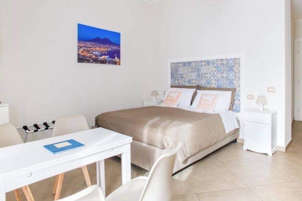 A hotel room with a bed, a desk, chairs, a nightstand, and a wall-mounted picture.