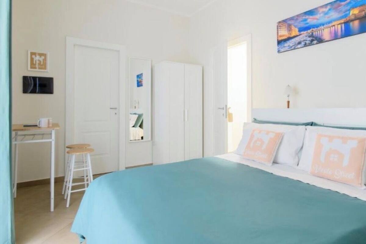 A bedroom with a bed, a desk, a chair, and a painting on the wall.