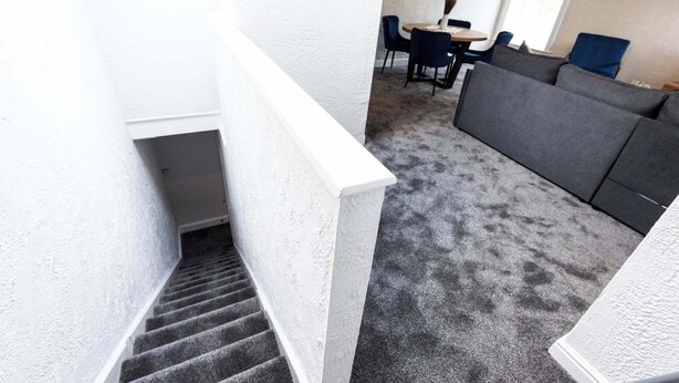 A staircase leading to a living area with a grey carpet, a grey sofa, and a dining table with chairs. - St Andrew's by Guestz (Lytham)