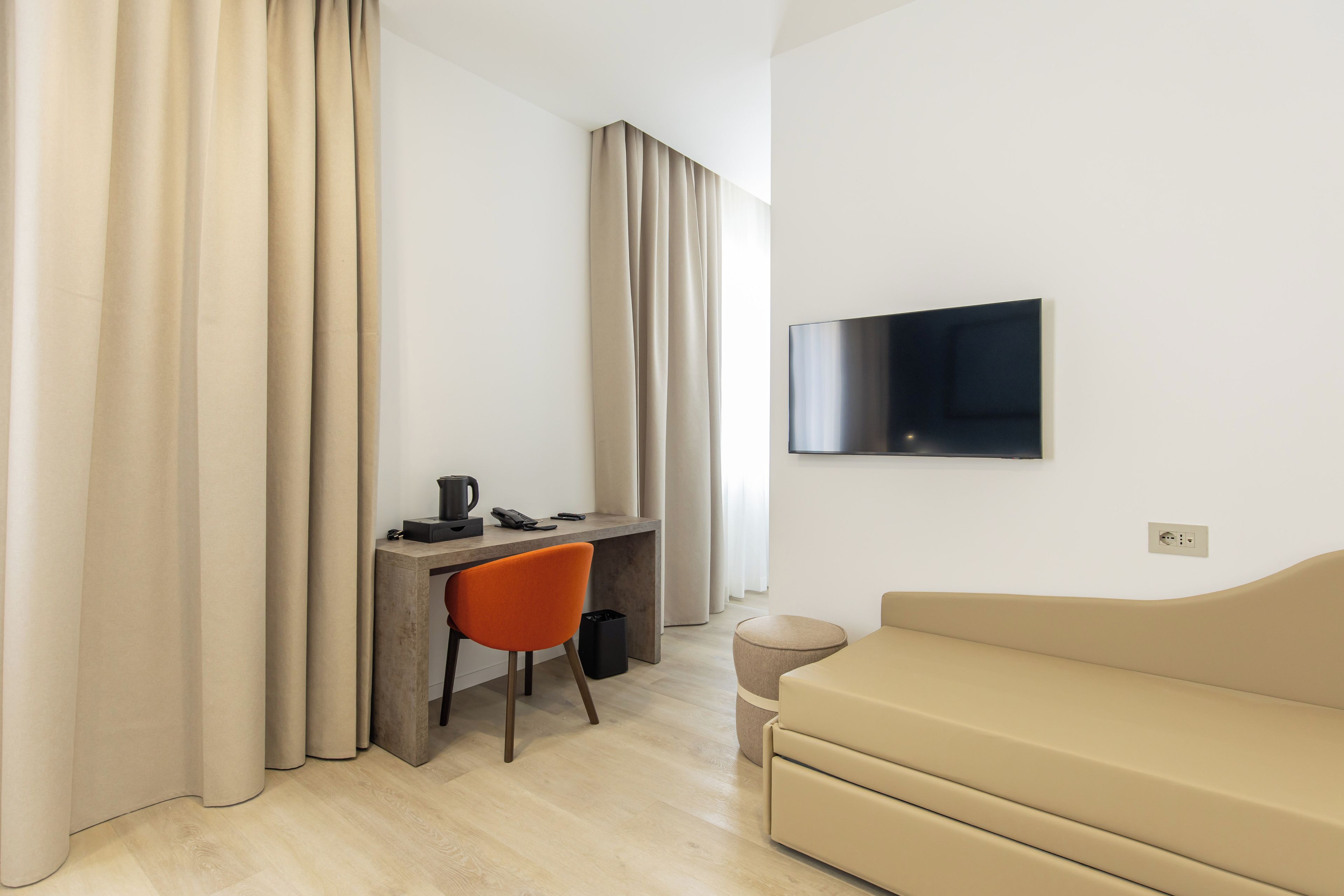 Une chambre d’hôtel moderne équipée d’un bureau, d’une chaise, d’un canapé et d’un téléviseur à écran plat fixé au mur.