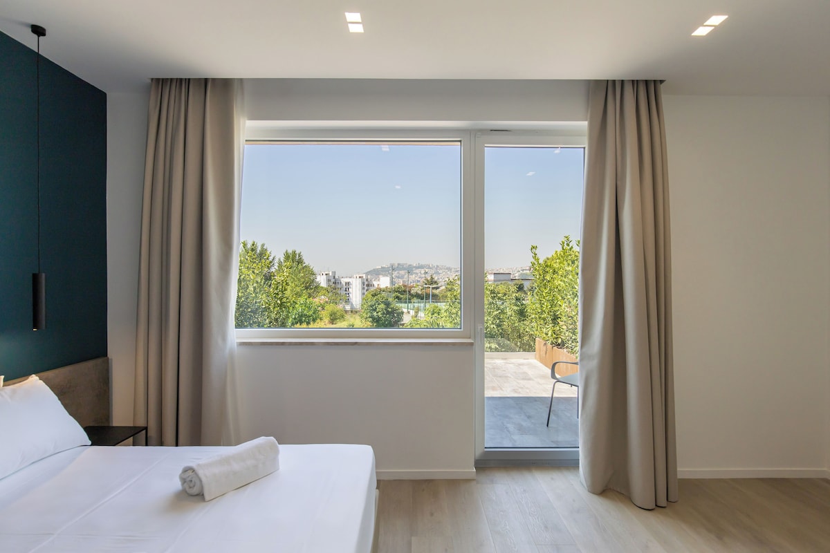 A hotel room with a bed, a large window, and a view of the cityscape.