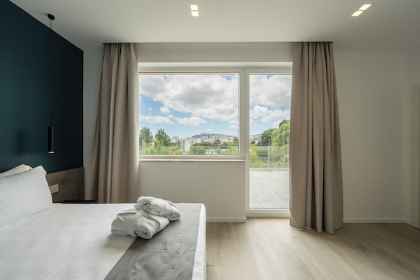 Ett hotellrum med en säng, utsikt över staden genom ett stort fönster och en balkong.