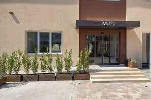 A modern building with a sign reading 'MU1' above the entrance. There are potted plants in front of the entrance and a paved area leading up to the door. - MU21 Hotel (Naples)