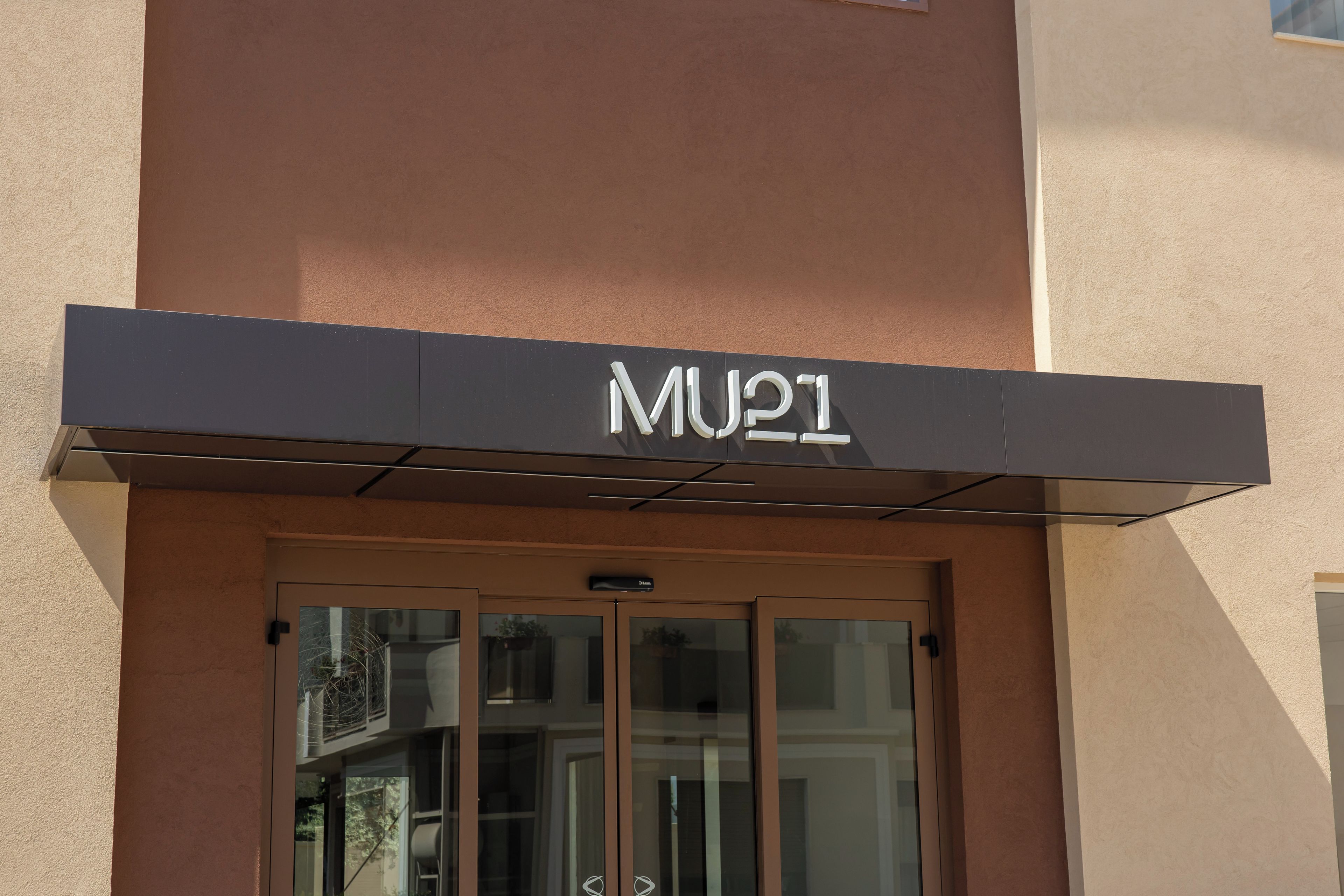 Une entrée d’immeuble avec une enseigne portant l’inscription « MU21 » au-dessus de la porte.