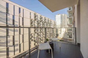 Ein Balkon mit Blick auf hohe Gebäude, einem Tisch mit Stühlen und einem kleinen Blumentopf.