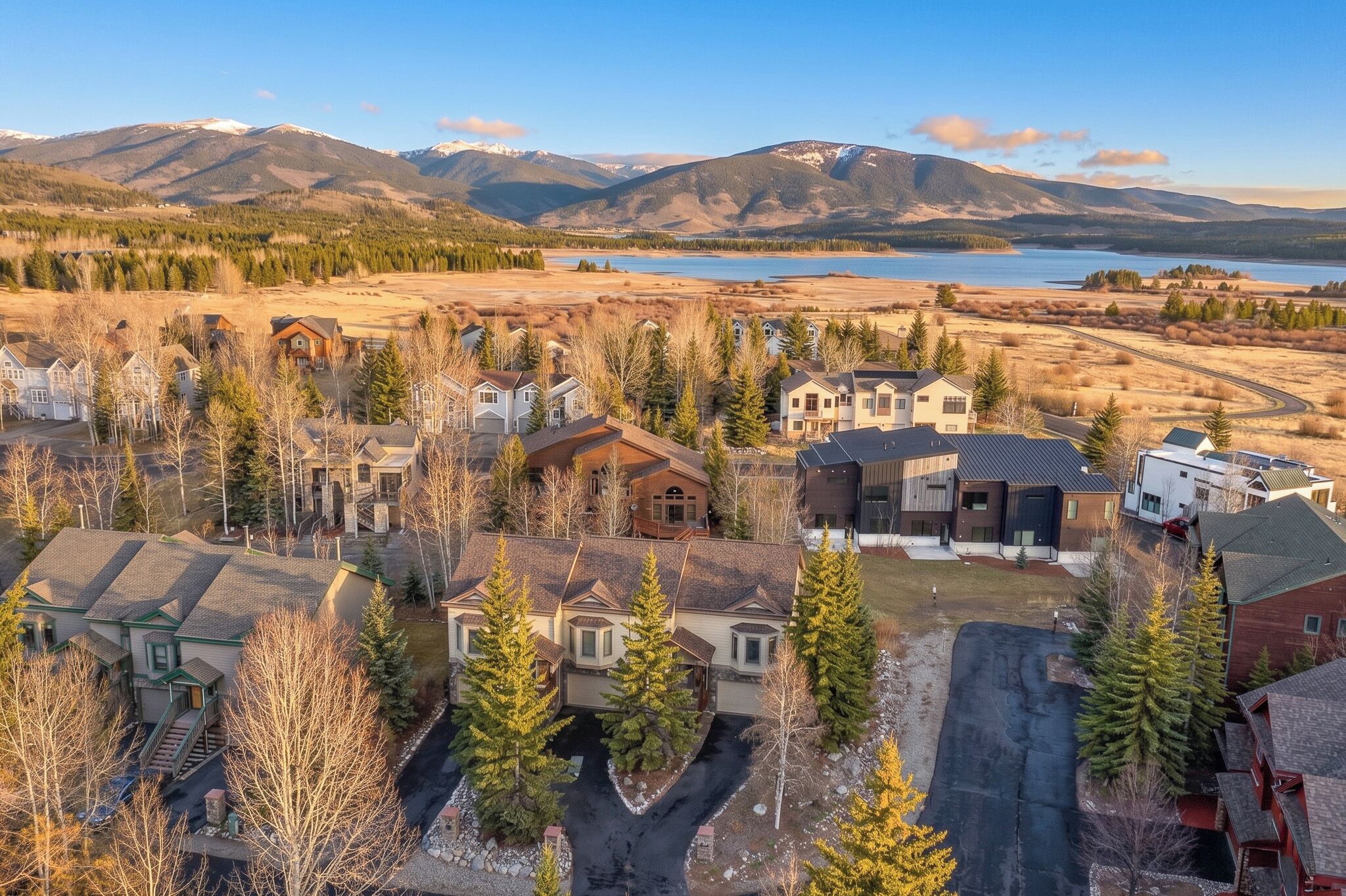 A residential area with houses, trees, and a lake with mountains in the background.