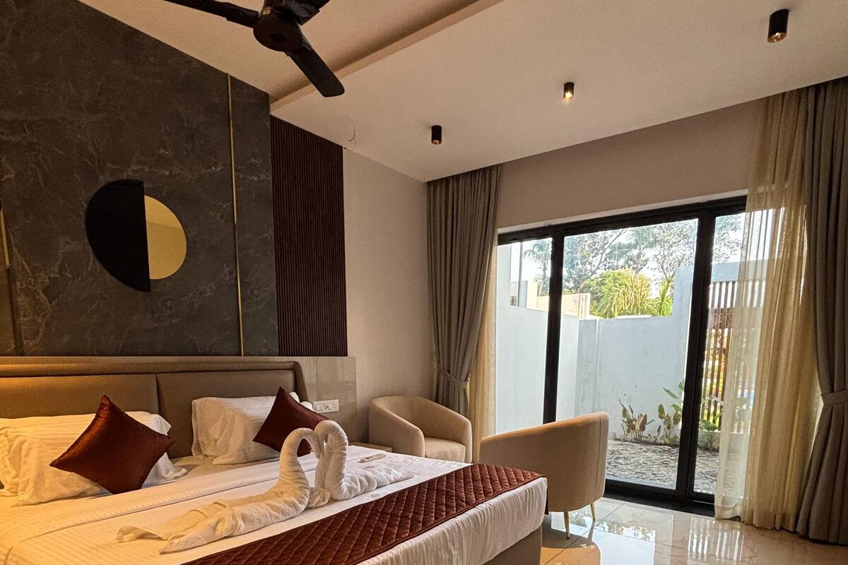 Une chambre d’hôtel moderne dotée d’un grand lit, d’un ventilateur de plafond, d’un coin salon avec un fauteuil et d’une vue sur l’extérieur grâce à une porte vitrée.