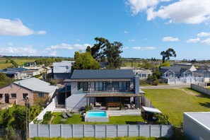 Et moderne hus i to etager med swimmingpool, omgivet af en indhegnet have og omkringliggende huse.