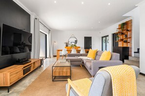 A modern living room with a flat-screen TV, a sofa with yellow cushions, a coffee table, and a wooden sideboard. - Cape Winelands Mountain View Getaway (Stellenbosch)