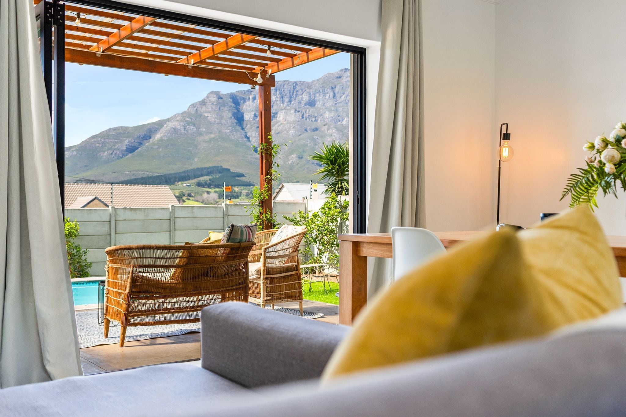A room with a view of mountains, a pool, and outdoor furniture.