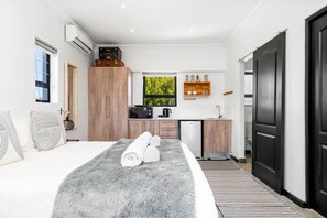 A modern bedroom with a large bed, a grey furry rug, and a view of a kitchen and bathroom. - Cape Winelands Mountain View Getaway (Stellenbosch)