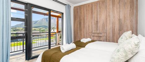 Habitación de hotel con cama, armario de madera y balcón con vistas al campo.