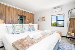 A modern bedroom with a large bed, wooden paneling, a view of the outdoors, and a small desk area. - Cape Winelands Mountain View Getaway (Stellenbosch)