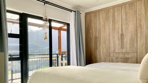 Een slaapkamer met een bed, een houten garderobe en een balkon met uitzicht op bergen.
