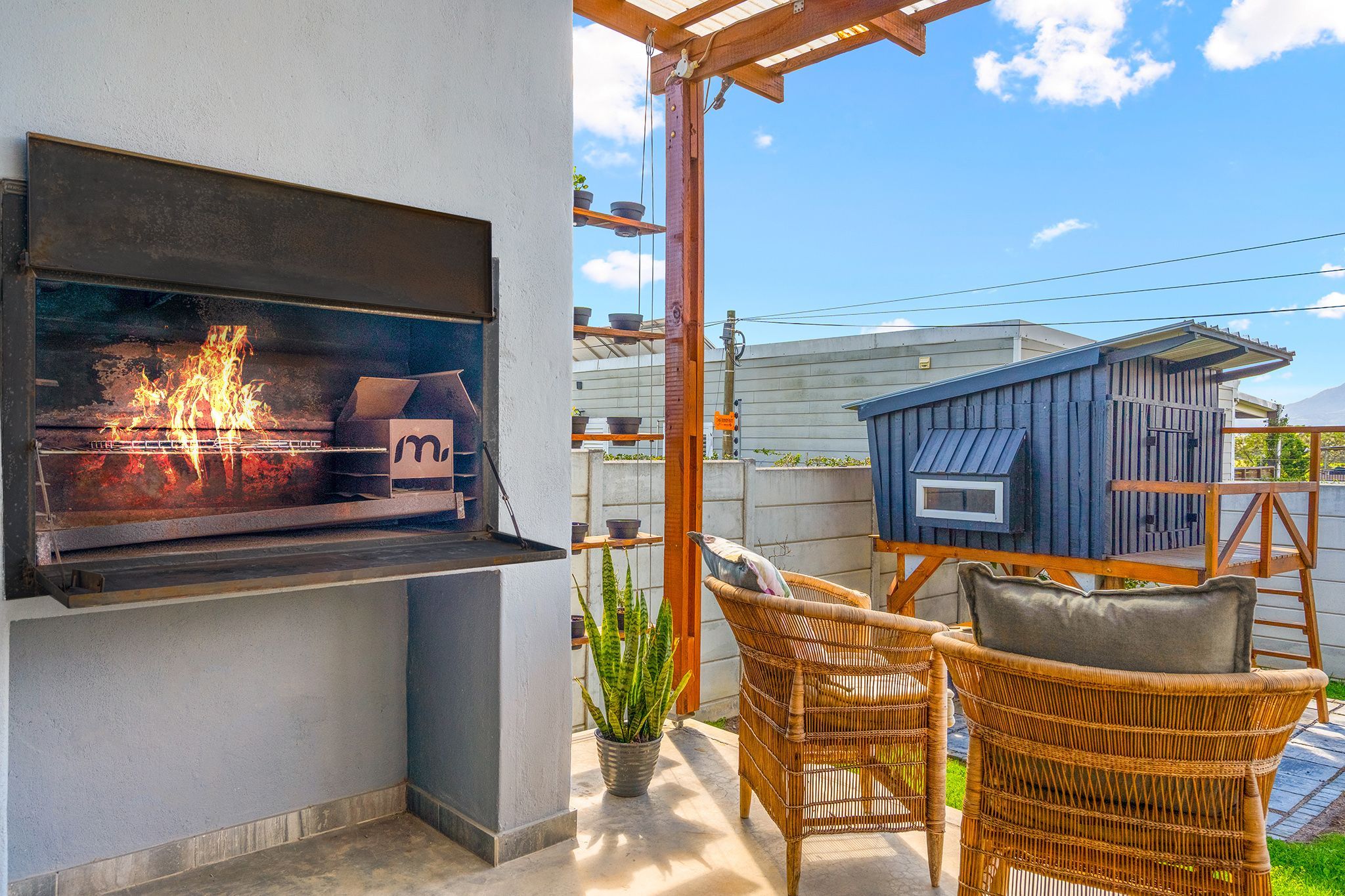 Una parrilla al aire libre con fuego, sillas de mimbre y un cobertizo azul pequeño.