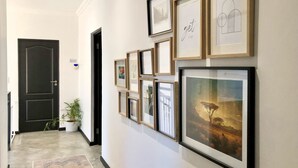 Een gang met ingelijste kunstwerken aan de muur, een kamerplant en een zwarte deur.
