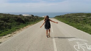 Una persona camina per una carretera amb carril bici, envoltada de verdura i amb vista al mar.